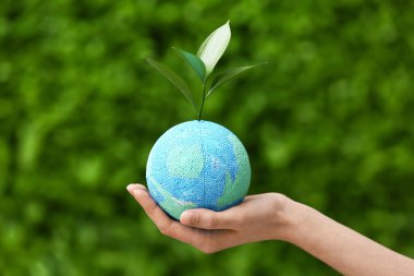 Yeşil çimen arka planında Dünya 'nın filizi ve maketi olan bir kadın eli. Dünya Çevre Günü
