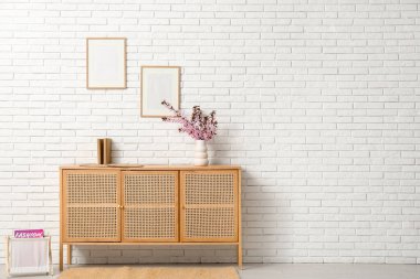 Oturma odasındaki beyaz tuğla duvarın yanında farklı bir dekor ve pembe çiçek açan vazo içeren bir elbise.