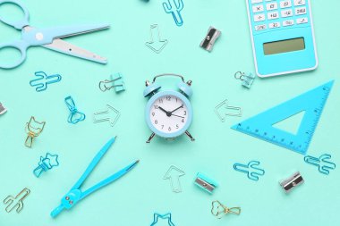 Alarm saati ve turkuaz arka planda farklı okul kırtasiyesine sahip kompozisyon