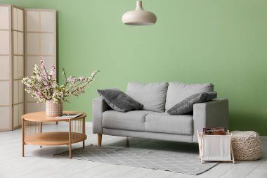 Kahve masalı kanepe, avize ve yeşil duvarın yanında çiçek açan vazo oturma odasında.