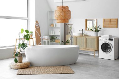 Küveti, büyük penceresi, ev bitkileri ve sörf tahtasıyla aydınlık banyonun içi.