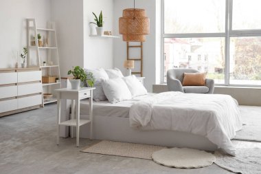 Yatak odasının içi rahat yatak odası, gri koltuk, ev bitkileri ve komodinlerle dolu.