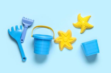 Kumsal kalıpları, mavi arka planda oyuncak tırmık ve kova.