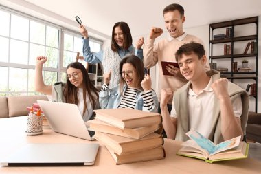 Kütüphanedeki masada dizüstü bilgisayarla çalışan bir grup mutlu öğrenci.