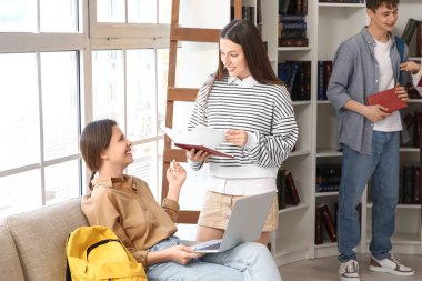 Diz üstü bilgisayar ve kitapla kütüphanede okuyan kız öğrenciler