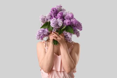 Gri arka planda, leylak çiçeklerinin arkasına saklanan güzel genç bir kadın.