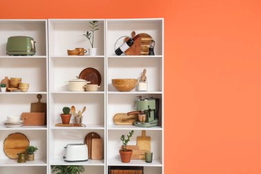 Mutfak gereçleri ve turuncu duvarın yanında bitkiler olan raf ünitesi.