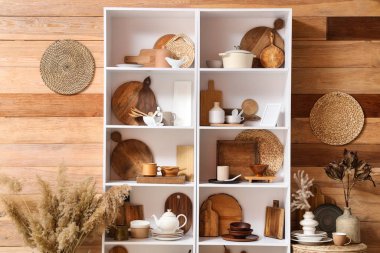 Mutfaktaki ahşap duvarın yanında mutfak aletleri ve tabakları olan raf ünitesi.