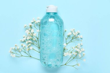 Bir şişe mikiler suyu ve mavi arka planda çiçekler.