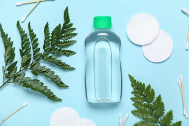 Bir şişe mikiler suyu, pamuk pedler ve mavi arka planda yapraklar.