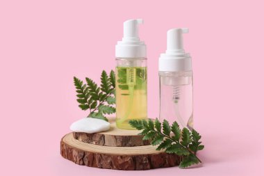 Pembe zemin üzerinde Micellar su, yapraklar ve pamuk pedi