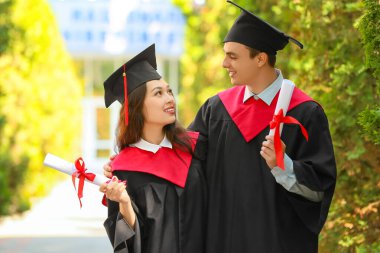 Diplomalı bir çift mezun öğrenci açık havada kucaklaşıyor.