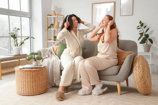 Evdeki kanepede müzik dinleyen, kulaklıklı güzel, genç, mutlu bayan arkadaşlar.