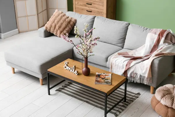 Sehpası, şifoniyeri ve yeşil duvarın yanında çiçek açan vazoları olan bir kanepe.