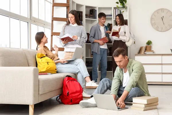 Bir grup öğrenci kütüphanede dizüstü bilgisayarlar ve kitaplarla çalışıyor.