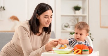 Bir kase lezzetli yemek, meyve ve sebzeyle beslenen mutlu anne evde küçük şirin bir bebek besliyor.