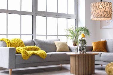 Işıl ışıl oturma odasının içinde rahat gri koltuklar, sehpa ve büyük pencerenin yanında parlayan lambalar.