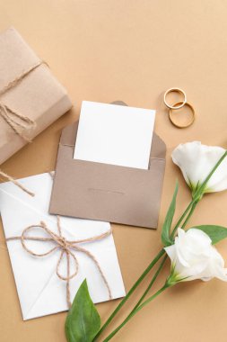 Hediye kutulu kompozisyon, boş kartlar, zarf, alyanslar ve bej arka planda güzel östoma çiçekleri.