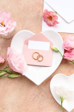 Zarflı kompozisyon, boş kart, alyans ve bej arka planda östoma çiçekleri.
