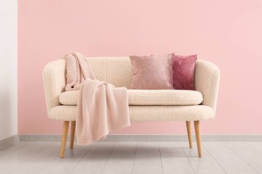 Pembe duvarın yanında yastıklı ve battaniyeli rahat kanepe.