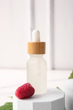 Beyaz arka planda bir şişe kozmetik ahududu yağıyla dekoratif podyum