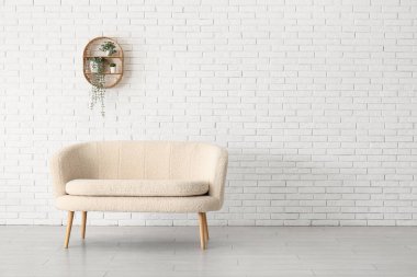 Rahat beyaz kanepe ve tuğla duvarın yanındaki bitkilerle dolu raflar.