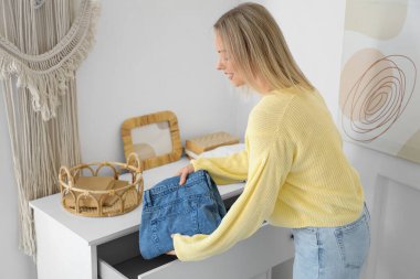 Katlanmış kotu evdeki çekmeceye koyan genç bir kadın.