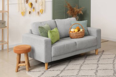 Gri kanepeli, sonbahar yapraklı ve sepetli balkabaklı oturma odasının içi.