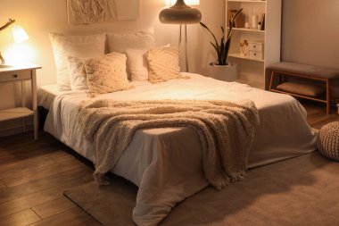 Rahat yatağın üzerinde yumuşak battaniyeler ve geceleri parlayan lambalar olan rahat yatak odasının içi.