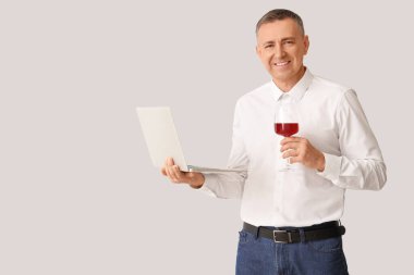 Beyaz arka planda bir bardak şarap ve dizüstü bilgisayarı olan yakışıklı bir adam.