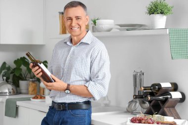 Mutfakta şarap şişesi olan yakışıklı olgun bir adam.
