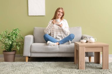 Evdeki kanepede çay içen genç bir kadın.