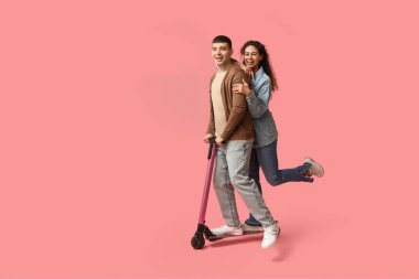 Pembe arka planda modern elektrikli scooter kullanan güzel bir çift.