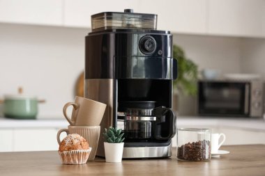 Modern kahve makinesi, fincanlar, kek ve fasulye kavanozu mutfakta.