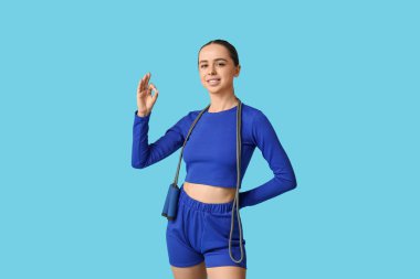 İp atlayan genç bayan antrenör mavi arka planda iyi bir hareket gösteriyor.