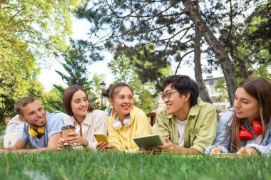 Elinde aletlerle parkta çim üzerinde yatan bir grup öğrenci.