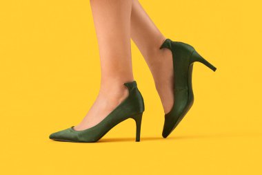 Sarı arka planda yeşil topuklu genç kadın bacakları