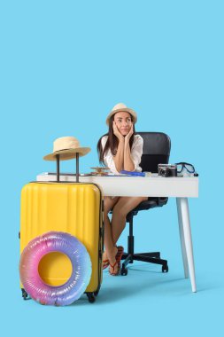 Masadaki genç iş kadını mavi arka planda yaz tatilini bekliyor.