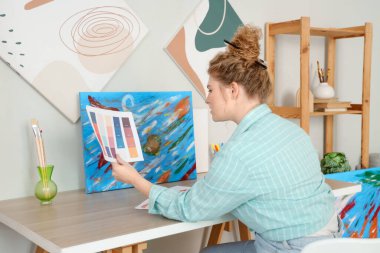 Atölyedeki masada boya rengi paleti olan kadın sanatçı.