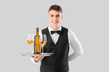 Tepside gri arka planda şarap taşıyan genç bir erkek garson.