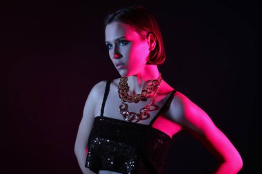 Koyu arkaplanda zarif zincirli bir kolye takmış şık bir genç kadın.