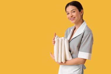 Sarı arka planda bir yığın temiz havlusu olan güzel bir oda hizmetçisi.