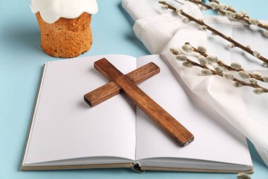 Söğüt dallı ahşap haç, Paskalya pastası ve mavi zemin üzerine boş kitap.