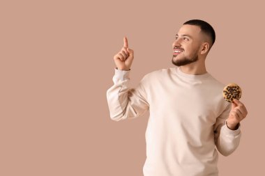 Kurabiyeli genç adam bej arka plandaki bir şeyi işaret ediyor.