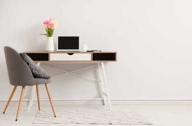 Modern dizüstü bilgisayarı ve beyaz duvarın yanında güzel çiçekleri olan şık çalışma alanı