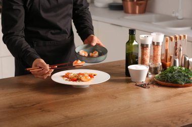 Erkek aşçı makarnanın üzerine karides koyuyor. Mutfakta, yakın plan.