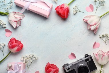 Güzel lalelerden yapılmış çerçeve, çingene çiçekleri, kağıt kalpler, hediye kutuları ve açık mavi arka planda fotoğraf makinesi. Anneler Günü kutlaması