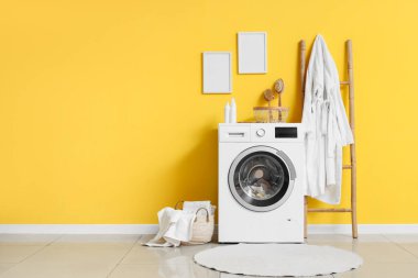 Modern çamaşır makinesi, hasır sepeti ve banyo aksesuarları olan şık bir çamaşırhane.