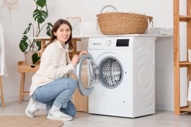 Çamaşır odasında çamaşır makinesi olan genç bir kadın.