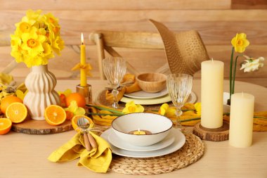 Narcissus çiçekleri, yanan mumlar ve taze portakallarla süslü zarif bir masa.